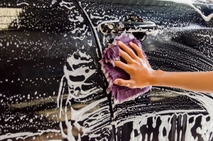 A Hand washing a car with a microfiber cloth