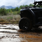 Štvorkolka prechádzajúca cez blatistý terén počas jazdy v prírode, ideálna pre off-road dobrodružstvá.